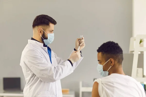 Arzt zieht Impfstoff aus Fläschchen, bevor er jungen Patienten Spritzen verabreicht — Stockfoto