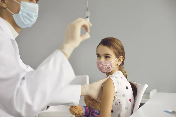 Szczęśliwa mała dziewczynka w masce, czekająca na szczepionkę w gabinecie lekarskim. — Zdjęcie stockowe