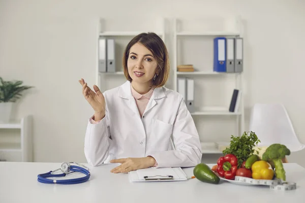 Nutritionist sitter vid skrivbordet på kliniken och berättar om fördelarna med hälsosam kost — Stockfoto