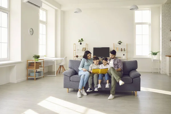 Keluarga bahagia duduk di sofa di apartemen studio modern dan membaca buku bersama — Stok Foto
