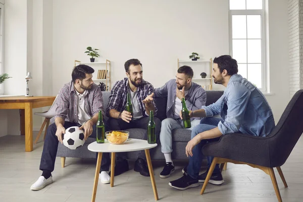 Группа мужчин, сидящих на диване, пьющих пиво, перекусывающих и обсуждающих футбольный матч — стоковое фото
