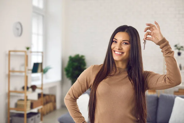 Happy young woman holding keys to her new house or apartment and smiling at camera