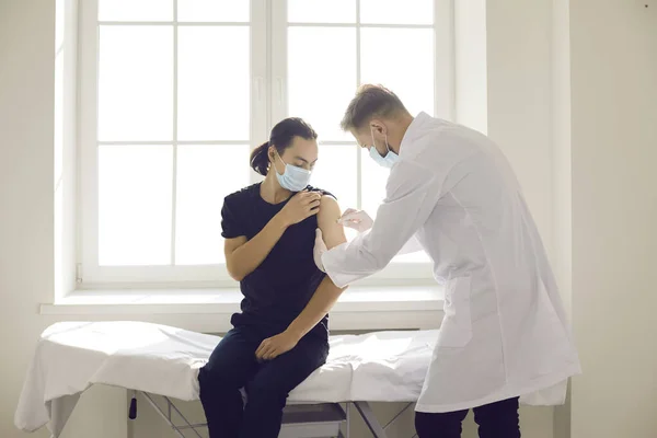 Üniformalı ve maskeli bir adam Asyalı hasta kolunu aşıya hazırlıyor. — Stok fotoğraf