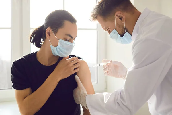 Медичний працівник в уніформі та масці для обличчя робить вакцинацію від ін'єкцій для азіатського чоловіка — стокове фото