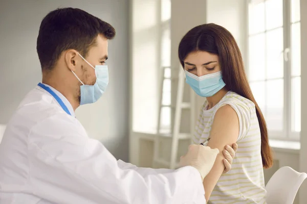 Enfermera masculina que da vacuna a una mujer joven durante la campaña de inmunización en el centro de salud — Foto de Stock