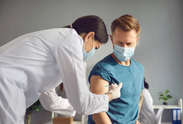 Fiatal nőorvos orvosi maszkban, 19 ncov fertőzés elleni vakcina beadásával férfi betegnek — Stock Fotó