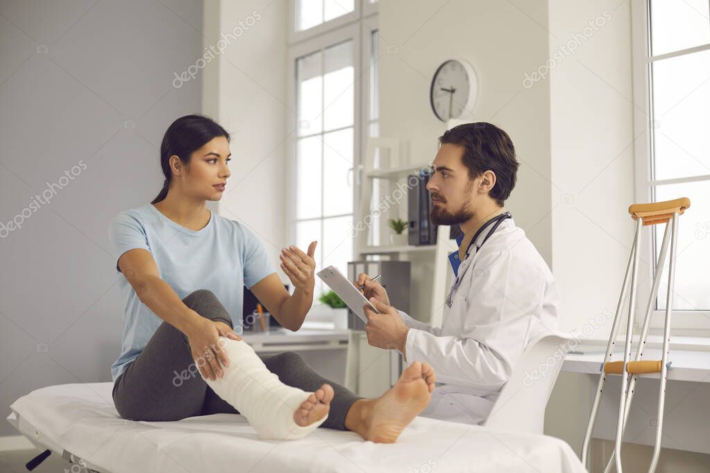 Young woman with leg fracture talking to doctor during medical exam at the clinic