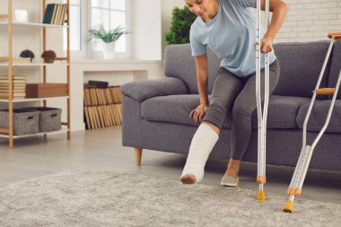 Kırık bacaklı genç kadın ayağa kalkıp koltuk değnekleriyle yürümeye çalışıyor.