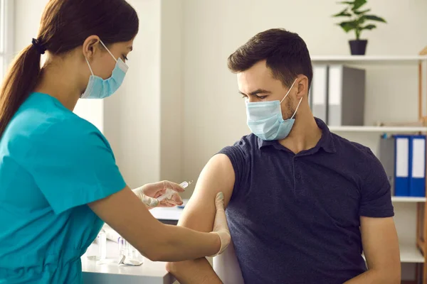 Klinikteki aşı kampanyası sırasında genç adama iğne yapan profesyonel hemşire. — Stok fotoğraf