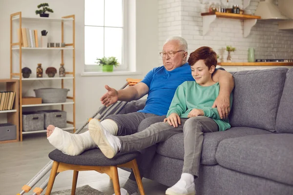 Oudere man met een gebroken been in een gips gips en vertelt kleinzoon het verhaal van hoe hij zijn enkel brak. — Stockfoto