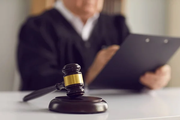 Close up de um martelo juízes sobre a mesa contra o pano de fundo de um juiz lendo o veredicto. — Fotografia de Stock