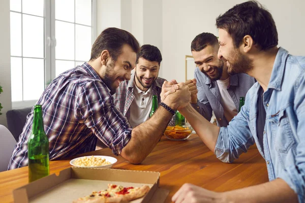 Groep vrienden kijken naar twee mannen arm-worstelen op fun party met pizza en bier — Stockfoto
