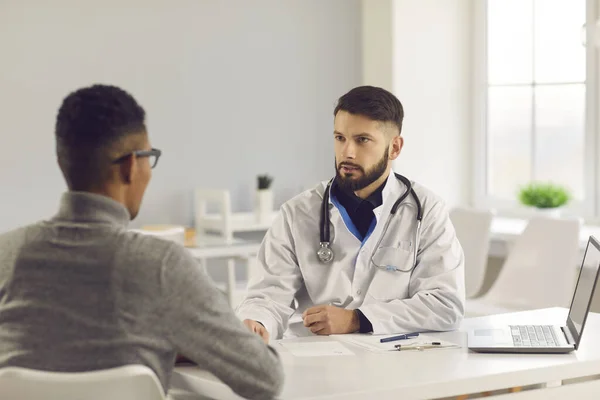 Arzt im Gespräch mit jungem Mann, erklärt, wie man Medikamente einnimmt und gesund bleibt — Stockfoto