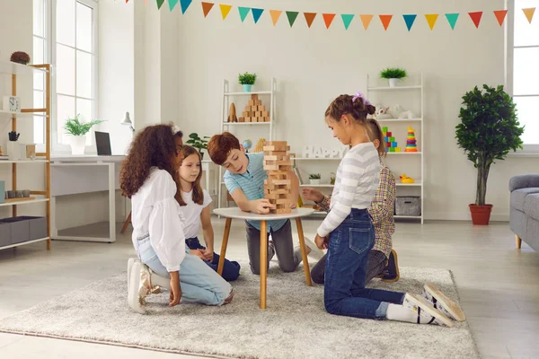 Group of quiet kids playing wood block tower stacking game at home or in leisure club — Stock Photo, Image
