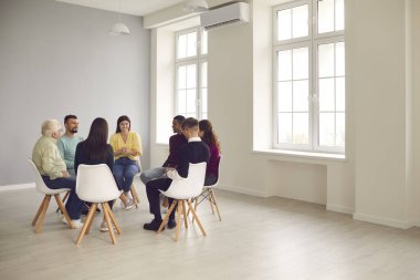 Çemberde oturan ve grup terapisinde dost canlısı terapistleri dinleyen farklı insanlar.