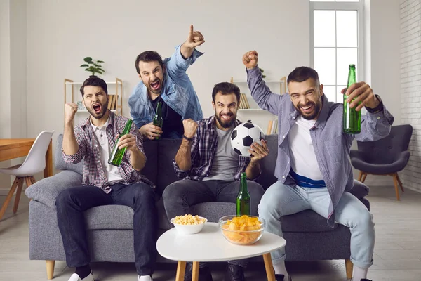 Захваченные друзья сидят на диване, смотрят футбольный матч и поддерживают любимую команду — стоковое фото