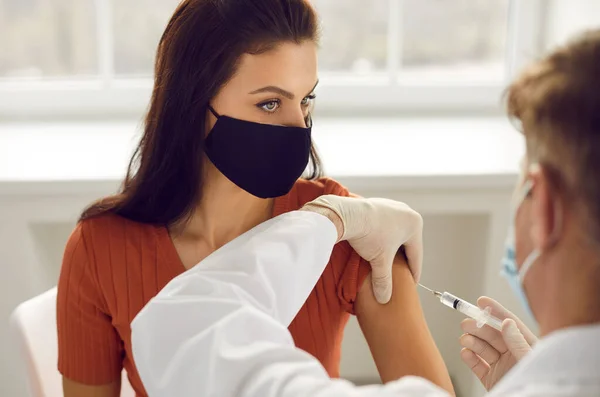 Woman in medical protective mask getting injection in arm vaccination against 19-ncov — Zdjęcie stockowe