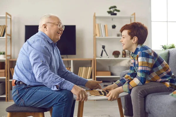 Vrolijke grootvader en kleinzoon spelen dammen en hebben plezier thuis — Stockfoto