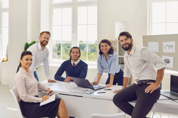 Skupina mladých usměvavých podnikatelů, kteří sedí v kanceláři a dívají se na fotoaparát při společné zahajovací diskusi — Stock fotografie