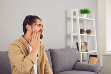Diş sinirleri iltihaplanmış ve yanağına acı içinde dokunan bir adam.