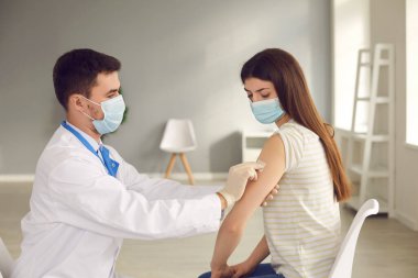 Doktor, hastaya mevsimsel grip enjekte ettikten sonra koluna yama uygular..