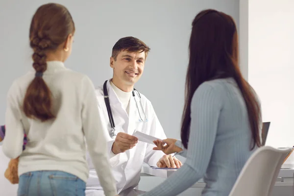 Médico sorridente que dá receita médica ou certificado de autorização para mãe e filha — Fotografia de Stock