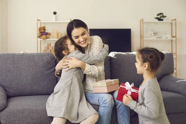 Szczęśliwa młoda kobieta przytula swoje dzieci i dziękuje im za prezenty w Dzień Matki — Zdjęcie stockowe