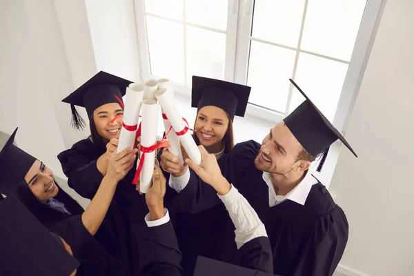 A multiracionális diplomások emelik a diplomájukat, és egymásra rakják őket az ablaknál az osztályteremben.. — Stock Fotó