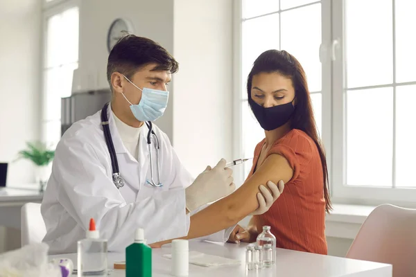 Manlig läkare i en medicinsk mask är på väg att injicera en injektion i en kvinnlig arm. — Stockfoto