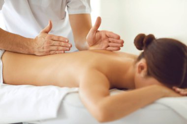 Bir masörün erkek eli masaj masasında yüz üstü yatan bir kadının sırtına masaj yapar..