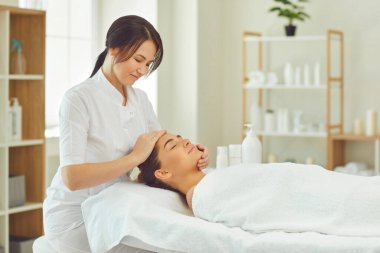 Gülümseyen masör, genç bir kadına elle masaj yapıyor.