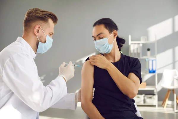 Pacjent pochodzenia azjatyckiego w masce do twarzy otrzymujący wstrzyknięcie szczepionki w celu ochrony przed zakażeniem 19-ncov — Zdjęcie stockowe