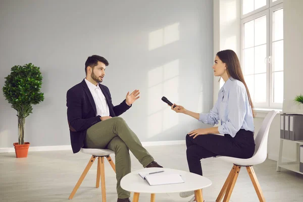 Mujer con un micrófono en la mano se sienta frente a un hombre famoso y lo entrevista. — Foto de Stock