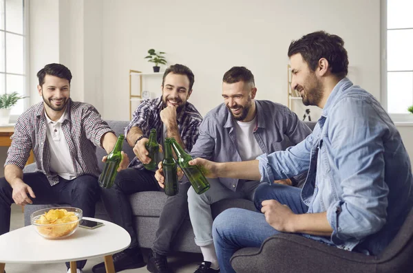 Groep vrienden zit op de bank, lachen en klappen bieren na grappige toast — Stockfoto