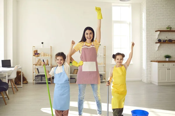 Мама з двома дочками прибирає в домі з піднятими руками прикидаючись супергероями.. — стокове фото