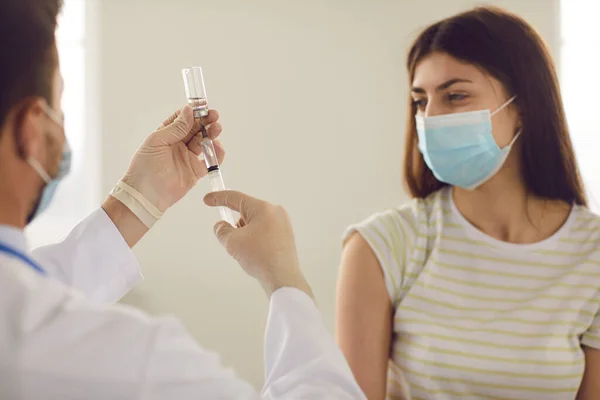 Kvinnlig patient i medicinsk ansiktsmask som tittar på läkare som fyller sprutan med vaccin — Stockfoto