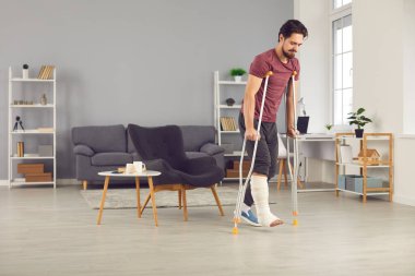 Kırık bacaklı bir adam koltuk değnekleriyle yürümeye çalışıyor ve iyi ilerleme kaydediyor.