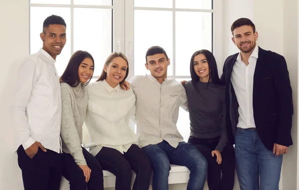 Group portrait of multiracial students sitting on the windowsill and hugging looking at the camera. — Stock Photo, Image