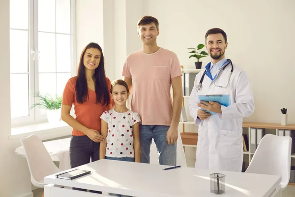 幸福的家人和他们的医生站在现代诊所的办公室里对着摄像机微笑 — 图库照片