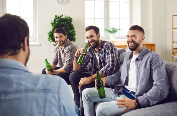 Groep gelukkige vrienden zittend op de bank in de woonkamer, bier drinkend en pratend — Stockfoto