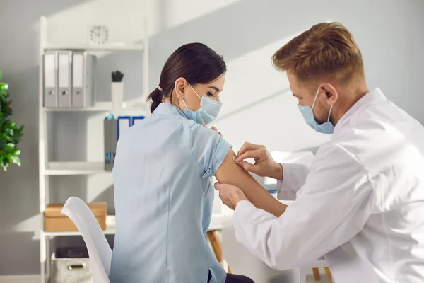 Mężczyzna pracownik medyczny przyklejający plaster medyczny do ramion kobiet po szczepieniu — Zdjęcie stockowe