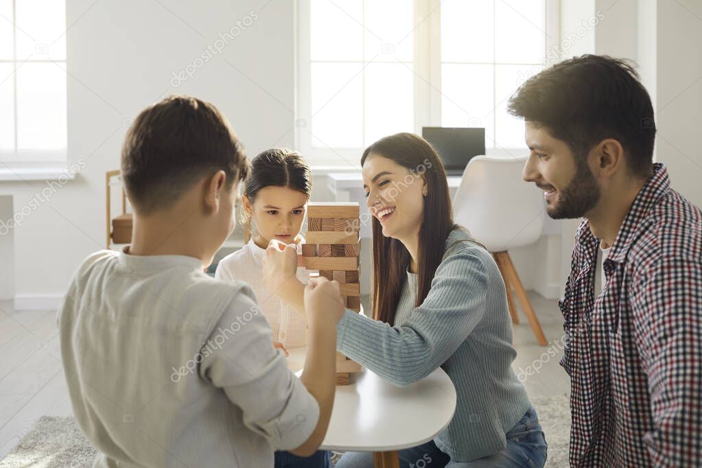 Happy young family plays with their children and take turns removing bricks from a wooden tower.