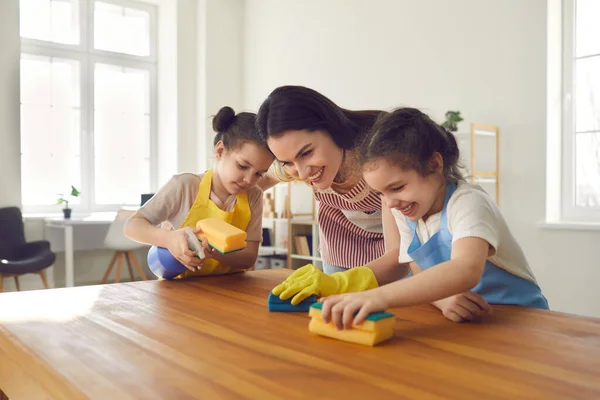 Amantes irmãs gêmeas ajudar a sua mãe carinhosa lavar a mesa da cozinha e limpar a casa. — Fotografia de Stock