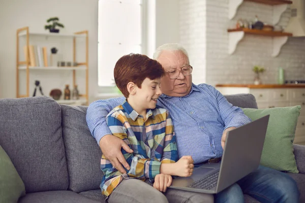Щасливий старий дід і маленький милий онук розважається вдома, використовуючи ноутбук, сидячи на дивані . — стокове фото