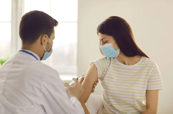 Young female patient looking at man doctor making vaccination against coronavirus infection — Stock Photo, Image