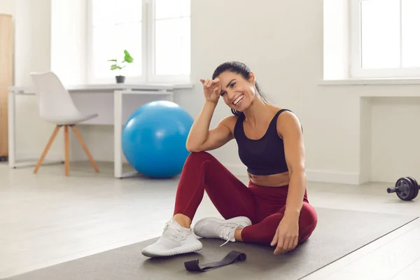 Mujer feliz descansando después de un entrenamiento de fitness exitoso y activo sentado en la alfombra deportiva en la habitación. —  Fotos de Stock