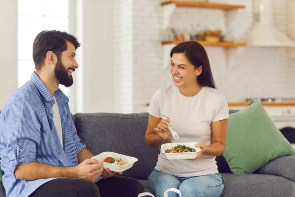 Jovem casal sorridente homem e mulher sentados em casa e comendo comida saudável em caixa — Fotografia de Stock