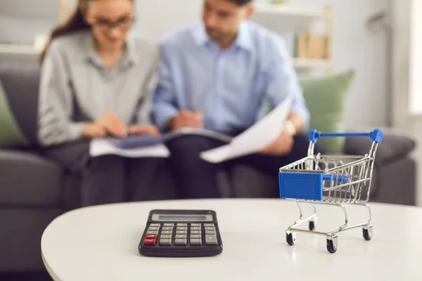 Calculadora e carrinho de compras de perto, casal calculando despesas em segundo plano — Fotografia de Stock