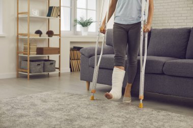 Yaralı bacağı alçıda olan kadın rehabilitasyon sırasında metal koltuk değnekleriyle ayakta duruyor.