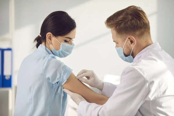 Man läkare i mask sätta plåster till kvinna patientarm efter coronavirus vaccination — Stockfoto